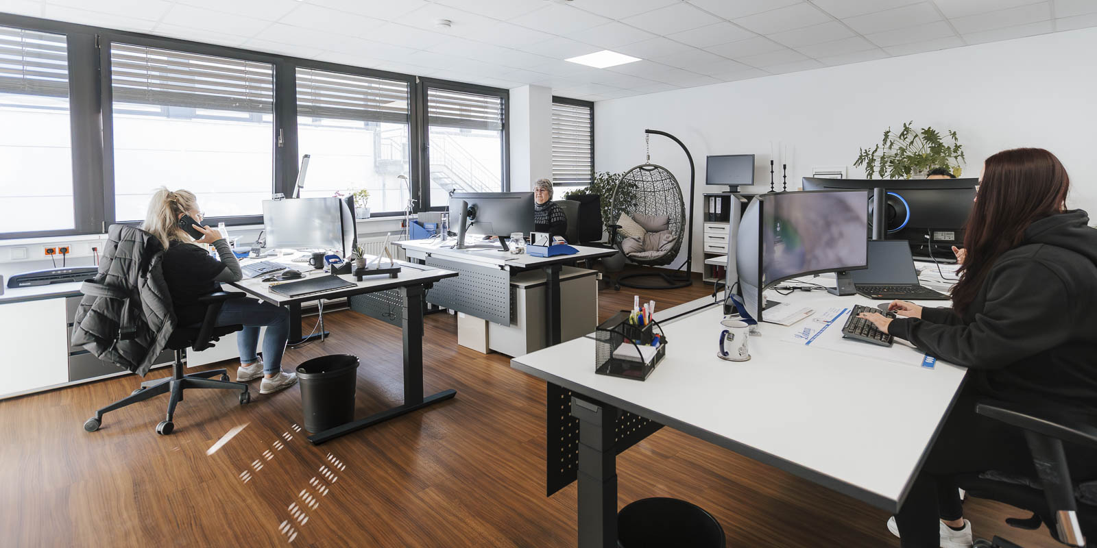 In einem modernen Büro arbeiten mehrere Personen an ihren Schreibtischen, während eine Frau am Telefon spricht.