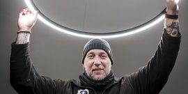 Ein Mann mit einem Bart und einem Mütze hebt seine Hände, um einen leuchtenden Ring über seinem Kopf zu halten.