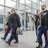 Die Gruppe von Technikern trägt verschiedene Werkzeuge und geht zielstrebig in einem modernen Gebäude mit Treppen und Aufzügen.