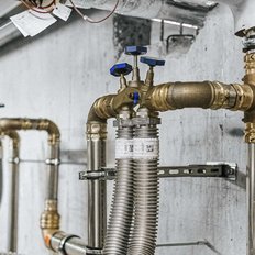 Eine komplexe Anordnung von Rohren und Ventilen an einer Betonwand, die für die Wasserversorgung in einem Gebäude ausgelegt ist.