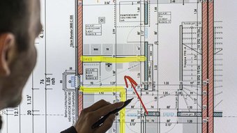 Auf dem Bildschirm ist ein technischer Plan zu sehen, während eine Person mit einem Stift wichtige Bereiche markiert.