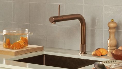 Eine moderne Küchenzeile mit einem eleganten Kupferwasserhahn und einem Glasbehälter voller geschnittener Süßkartoffeln.