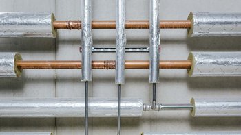 Eine Anordnung von isolierten Rohren an einer Wand, die verschiedene Materialien wie Kupfer und Metall zeigen.