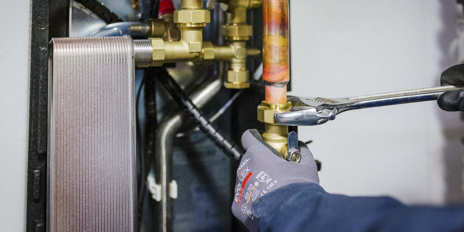 Ein Handwerker arbeitet mit einem Schraubenschlüssel an einer Heizungsinstallation, um eine Verbindung zu sichern.