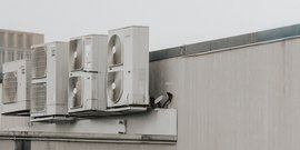 Auf einem Dach sind mehrere Klimaanlagen installiert, die in einer Reihe angeordnet sind und eine graue Wand im Hintergrund haben.