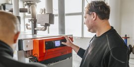 Ein Techniker bedient ein modernes Heizgerät, während ein Kollege im Hintergrund zuschaut und die Einstellungen überprüft.