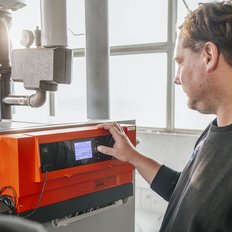Ein Techniker bedient ein modernes Heizgerät, während ein Kollege im Hintergrund zuschaut und die Einstellungen überprüft.