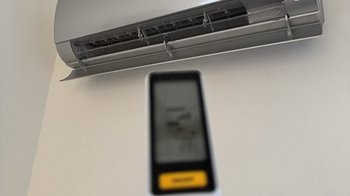 Die Fernbedienung wird auf eine Klimaanlage gerichtet, die an der Wand montiert ist und eine grüne Betriebsanzeige zeigt.