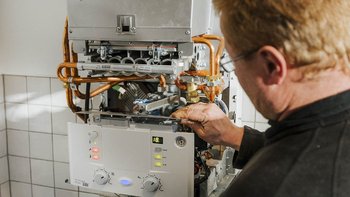 Ein Techniker arbeitet an einer Heizungsanlage, während er mit einem Werkzeug an der Steuerungseinstellung hantiert.