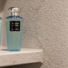 Zwei Flaschen Shampoo und Conditioner stehen auf einem hellen Regal, umgeben von einer schlichten, strukturierten Wand.