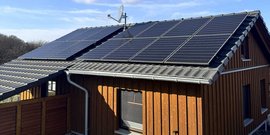 Ein modernes Haus mit einem schrägen Dach, das mit Solarpanelen und einer Satellitenschüssel ausgestattet ist.