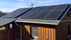 Ein modernes Haus mit einem schrägen Dach, das mit Solarpanelen und einer Satellitenschüssel ausgestattet ist.