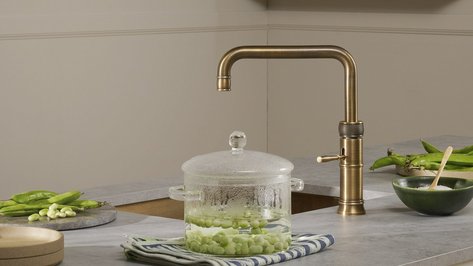 Eine elegante Küchenzeile mit einem goldenen Wasserhahn und einem Glasbehälter, der grüne Bohnen enthält.