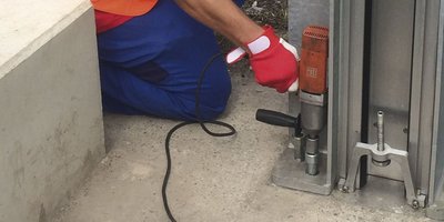 Ein Arbeiter in orangefarbener Kleidung benutzt ein Werkzeug, um eine Metallstruktur auf einem Betonboden zu befestigen.