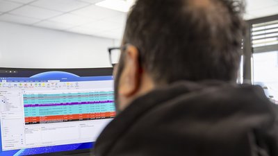Ein Mann mit Brille sitzt vor einem Computerbildschirm, auf dem bunte Daten und Tabellen angezeigt werden.