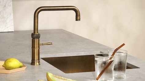Eine elegante, bronzefarbene Armatur steht auf einer modernen, grauen Arbeitsplatte neben zwei Gläsern mit kaltem Wasser.