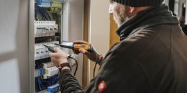 Ein Elektriker überprüft sorgfältig die Verkabelung in einem Sicherungskasten mit einem Messgerät in der Hand.
