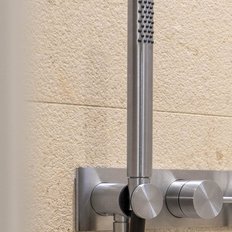 Eine moderne Duscharmatur aus Edelstahl mit drei Drehknöpfen an einer hellen, strukturierten Wand.