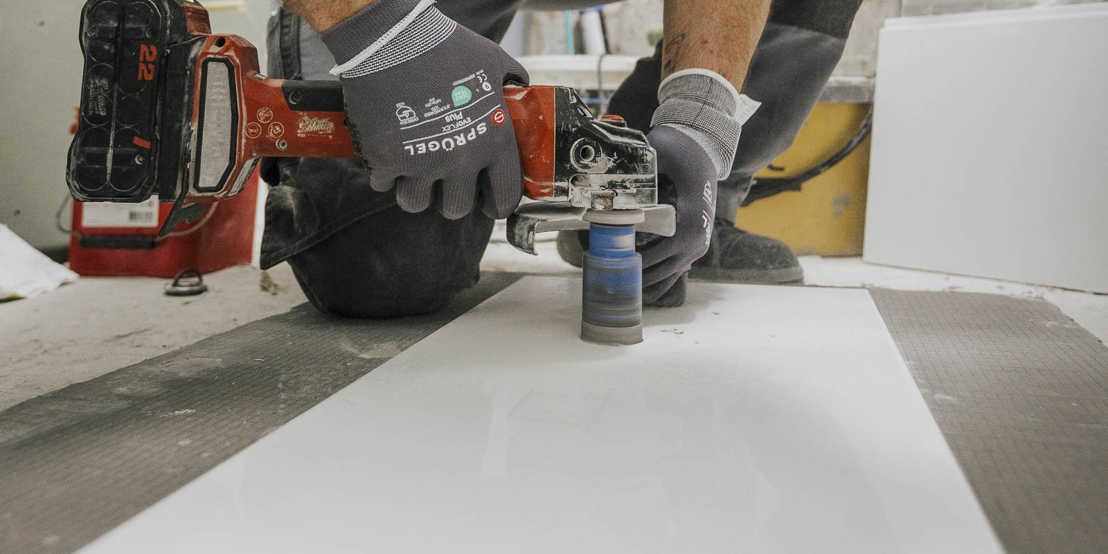 Ein Handwerker benutzt eine elektrische Maschine, um präzise Schnitte auf einer weißen Platte zu machen, während er konzentriert arbeitet.