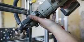 Eine Hand hält ein Werkzeug, während sie eine Metallarmatur an einer Konstruktion befestigt, um eine Installation vorzunehmen.