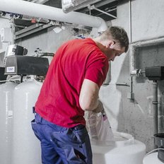 Ein Arbeiter in einem roten Shirt füllt einen Behälter in einem technischen Raum mit einer weißen Substanz.