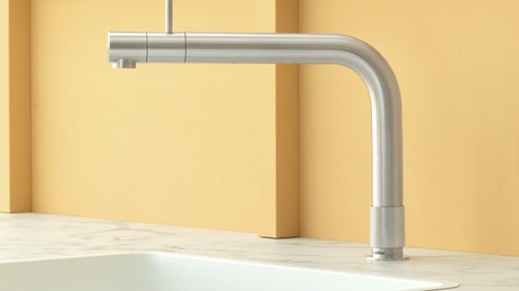 Ein eleganter, gebogener Wasserhahn aus Edelstahl steht vor einer sanften, orangefarbenen Wand, die Wärme ausstrahlt.