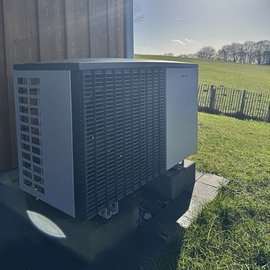Eine moderne Klimaanlage steht auf einem Betonfundament, umgeben von grünem Gras und einem klaren blauen Himmel.