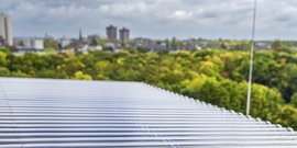 Ein Blick auf ein modernes Dach mit Metallstreifen, während die Stadt und grüne Bäume im Hintergrund sichtbar sind.