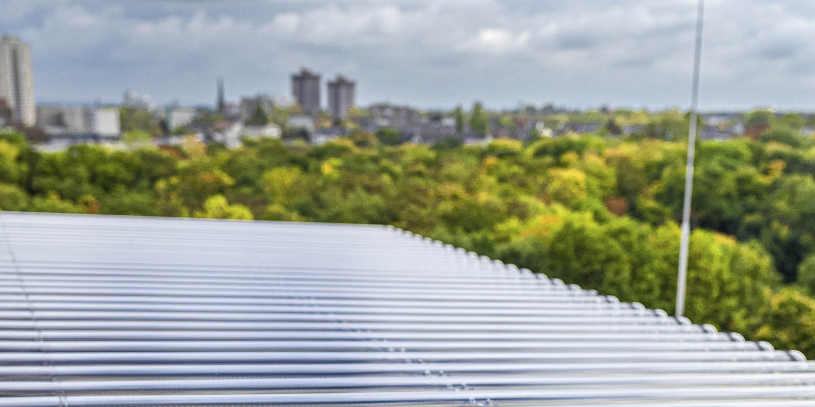 Ein Blick auf ein modernes Dach mit Metallstreifen, während die Stadt und grüne Bäume im Hintergrund sichtbar sind.