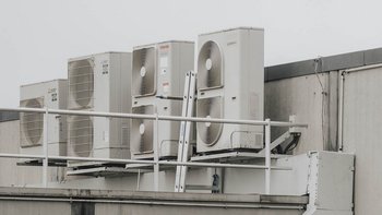 Auf einem Dach sind mehrere Klimaanlagen installiert, die in einer Reihe angeordnet sind und eine graue Wand im Hintergrund haben.