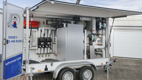 Ein mobiler Technikcontainer mit verschiedenen Rohren und Geräten, der auf einem gepflasterten Platz steht.