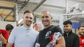 Zwei Männer stehen in einem Geschäft, lächeln und halten Geschenke mit roten Schleifen in den Händen.