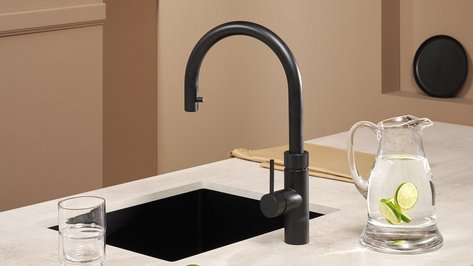 Ein eleganter schwarzer Wasserhahn steht über einem modernen Spülbecken, während ein Krug mit Limettenwasser daneben platziert ist.