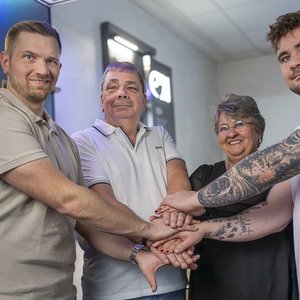 Vier Personen stehen zusammen und legen ihre Hände übereinander, was Teamgeist und Zusammenhalt symbolisiert.