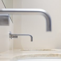 Zwei moderne Wasserhähne aus Edelstahl sind an einer hellen Wand montiert, mit einem eleganten Waschbecken im Vordergrund.