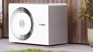 Eine weiße Klimaanlage steht neben einer Holzverkleidung, umgeben von grünen Pflanzen und einem ruhigen Außenbereich.