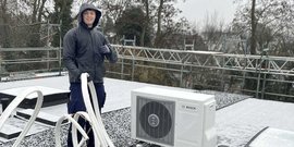 Ein junger Mann steht auf einem schneebedeckten Dach und zeigt mit dem Daumen nach oben, während er eine Klimaanlage installiert.