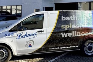 Der weiße Lohmar-Lieferwagen zeigt eine auffällige Werbung für Wellness und Bäder auf seiner Seite, während er geparkt ist.