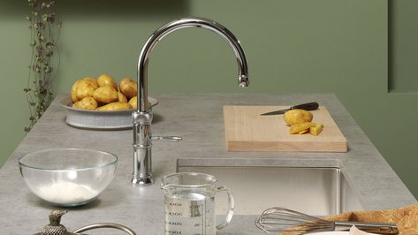 Eine moderne Küchenszene mit einem glänzenden Wasserhahn, frischen Kartoffeln und einem Holzbrett mit geschnittenem Gemüse.