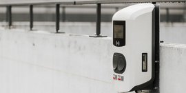 Eine moderne Ladestation für Elektrofahrzeuge, die an einer Betonwand montiert ist, mit zwei Ladeanschlüssen und einem Display.
