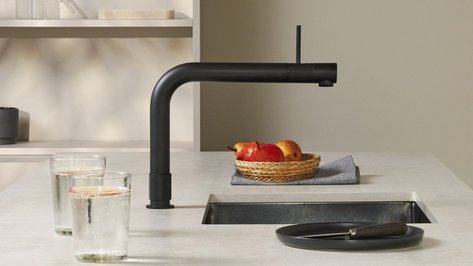 Ein moderner Küchentisch mit einem schwarzen Wasserhahn, zwei Gläsern mit Zitrone und einem Korb voller Äpfel.