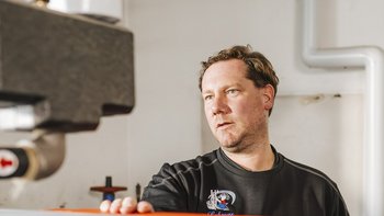 Ein Mann in einem schwarzen Shirt arbeitet konzentriert an einer Maschine in einer hellen Werkstatt.