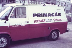 Ein älterer Transporter mit der Aufschrift 'Lohmar Sanitär Heizung' steht an einer belebten Straße, umgeben von weiteren Autos.