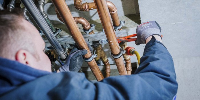 Ein Handwerker arbeitet konzentriert an Kupferrohren, während er eine Zange benutzt, um eine Verbindung zu sichern.