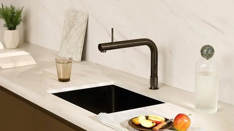 Eine moderne Küchenzeile mit einem eleganten Wasserhahn, frischen Äpfeln und einer stilvollen Glasflasche auf der Arbeitsplatte.