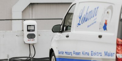 Eine moderne Ladestation für Elektrofahrzeuge ist an einer Wand montiert, neben einem weißen Lieferwagen mit Firmenbeschriftung.