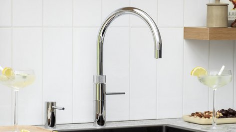 Ein eleganter Wasserhahn mit geschwungener Form steht über einer modernen Spüle, umgeben von stilvollen Gläsern und Snacks.