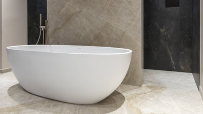 Eine elegante, freistehende Badewanne aus weißem Material steht auf einem marmorierten Boden in einem modernen Badezimmer.