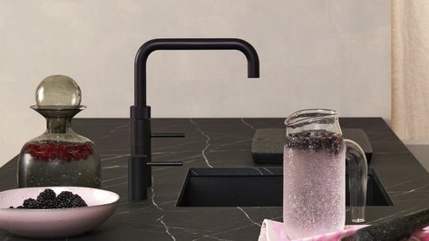 Ein eleganter Küchentisch aus schwarzem Marmor mit einer modernen Wasserarmatur und frischen Beeren in einer Schüssel.