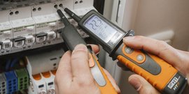 Ein Techniker misst mit einem Multimeter die Spannung in einem elektrischen Verteilerkasten.
